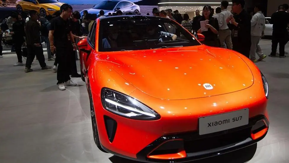 A bright orange Xiaomi SU7 sedan displayed at a Xiaomi booth at the National Exhibition Center in Shanghai, China in April 2025.