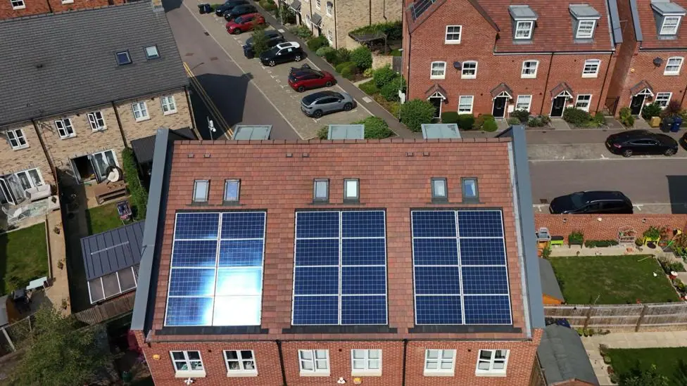 Aerial view of semi-detached and homes and terraced houses with solar panels installed. In the background are a series of avenues with cars parked up and small green lawns.