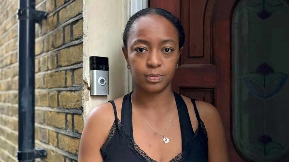 Woman wearing black top looks at camera in front of doorbell and front door