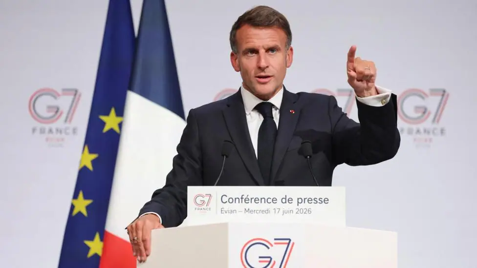 French President Emmanuel Macron holds a press conference during the G7 Summit, he speaks at a lectern and points with one hand.