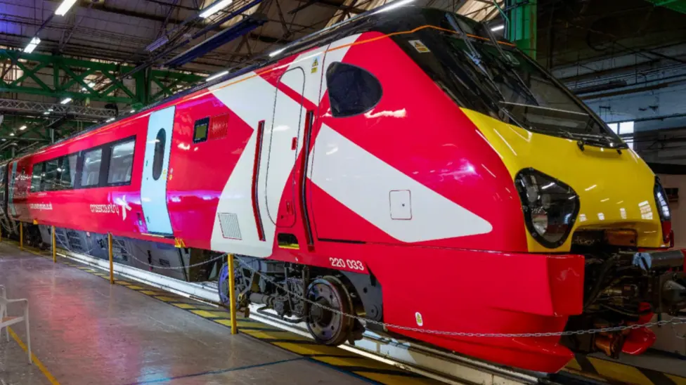 An image of a refurbished CrossCountry Voyager train inside a warehouse at a launch event. The train is mainly red, with a white X, which is partially on the driver's door.
