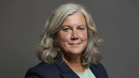 Transport Secretary Heidi Alexander wears a navy blazer and green top. She is smiling at the camera.