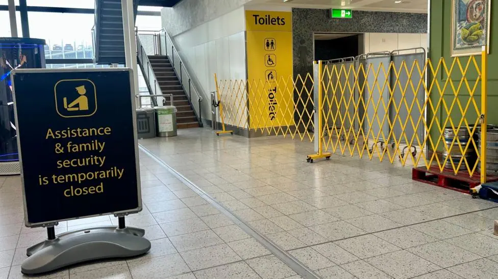 a yellow barrier is seen across an area marked Toilets, behind a sign saying 'Assistance & family security is temporarily closed'