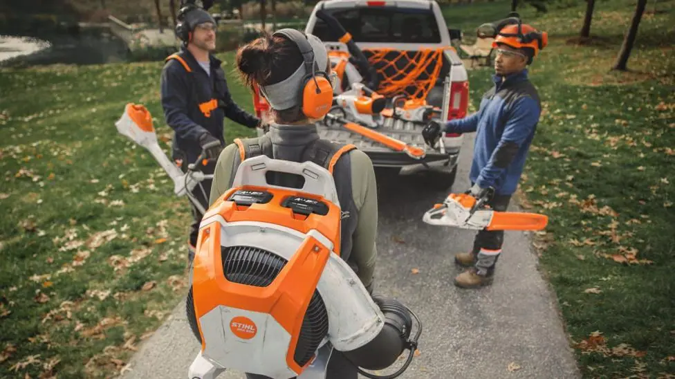 A marketing shot from Stihl shows three people carrying electric landscaping kit.