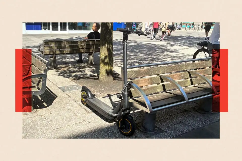 A black privately owned e-scooter locked with a D-lock to a bench on a pavement in Southampton.