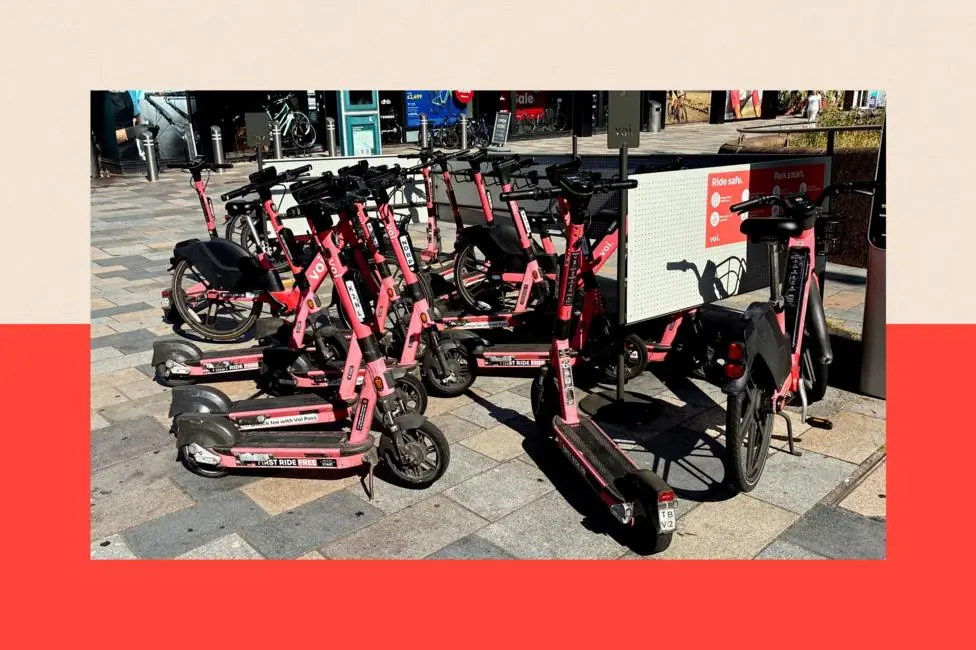 A designated e-scooter parking spot in Southampton. The orange e-scooters are parked on a pavement next to some railings. A sight reads: "Ride safe."