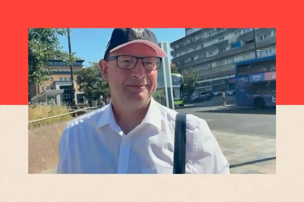 Photo showing Keith Reed. He is a white man wearing a baseball cap, dark-rimmed glasses and an open-necked white shirt. Behind him a street in Southampton is visible, with two buses going past.