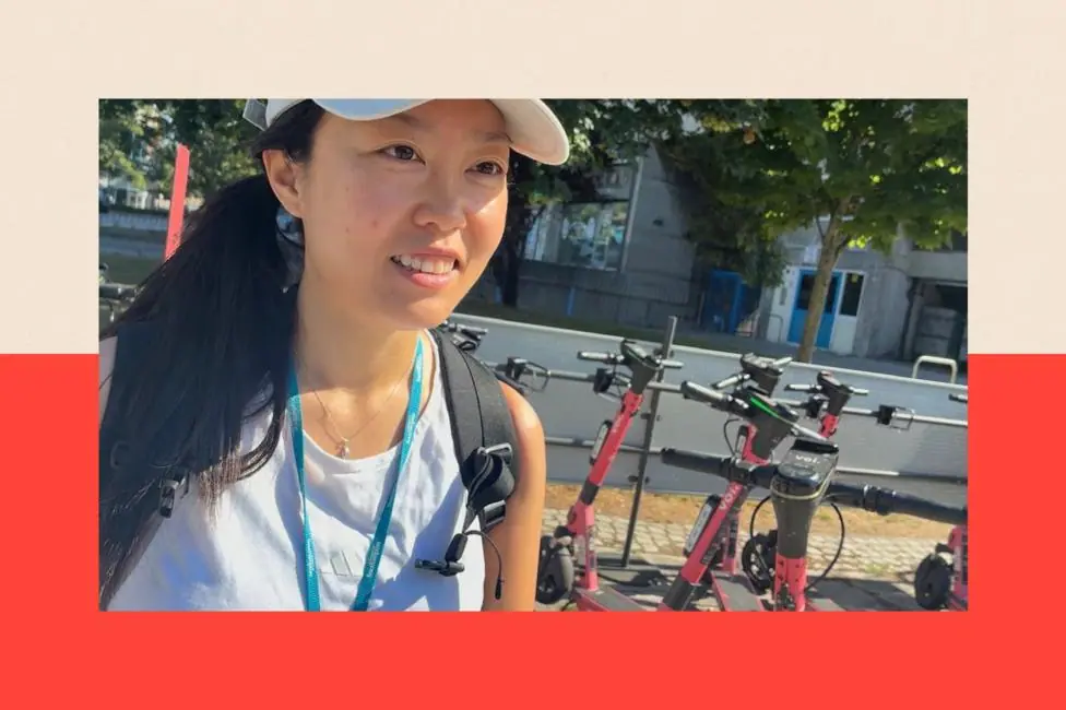 A picture shows Yan Zhang in the left of the frame. She is an Asian woman wearing a white baseball cap and a sleeveless light blue top. Behind on the right of the frame, a group of hire e-scooters…