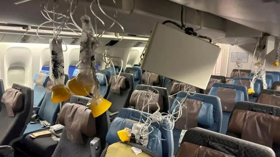 Oxygen masks hang from the ceiling inside an aircraft cabin. Rows of seats sit empty beneath them.