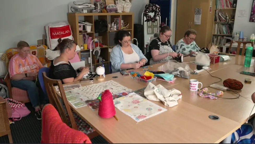 A group of women sat around a table knitting and sewing.