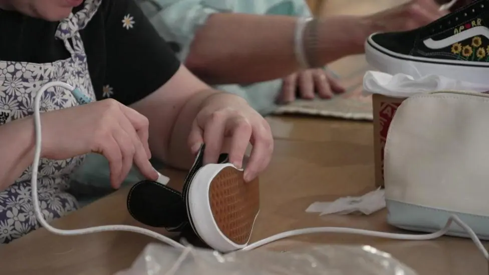 Someone holds a glue gun against a black Converse-like shoe.