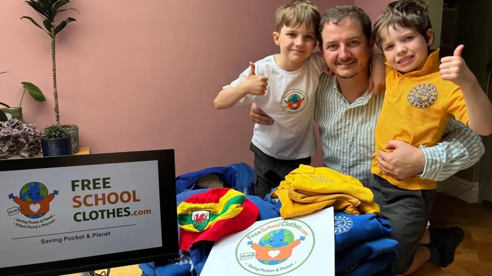 Jon who is 42 is pictured with his two children 10 year old Tom and six year old, Sion in amongst several blue school jumpers and several yellow polo shirts from Ysgol Treganna primary school next to…