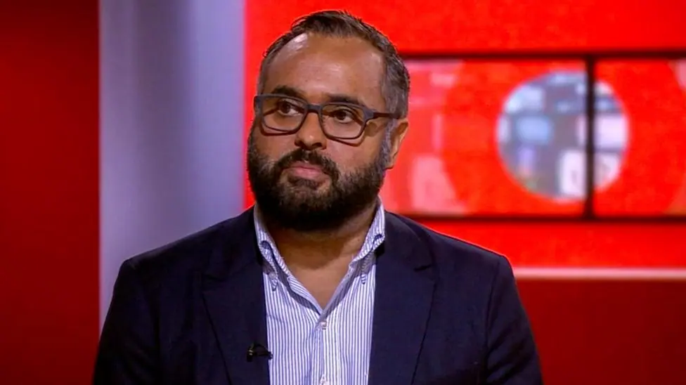 Marc Cieslak is pictured in the BBC newsroom. He is wearing glasses, a navy jacket and a blue striped shirt