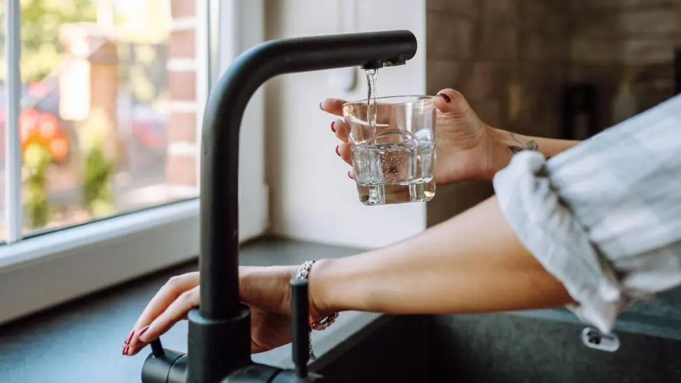 Hands only image of someone turning on a mixer tap to fill a glass of water