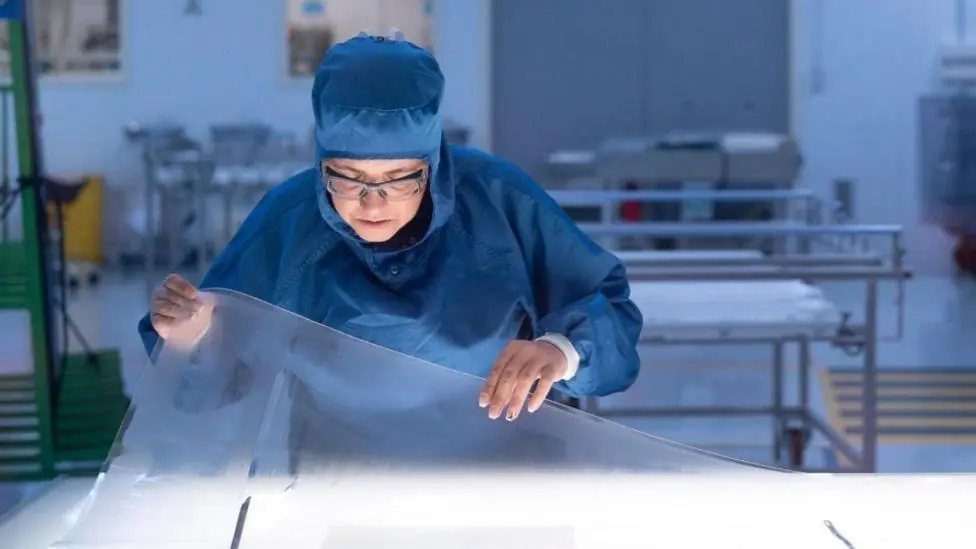 A Saint-Gobain worker in a darkened room works on a clear sheet of acrylic.