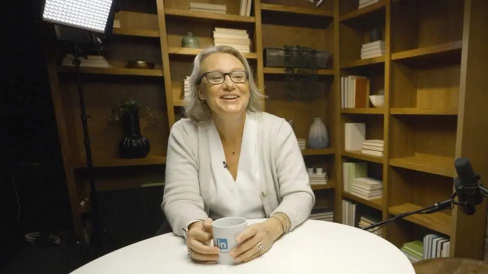 Nicole Leverich sitting at a table in a podcast studio with a mug on the table