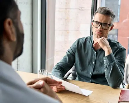 Serious businessman holding CV listening to applicant at job interview