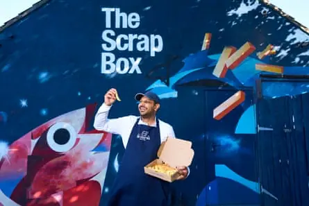 Beside a mural of a huge fish and some chips, Gavin holds up a chip from a takeaway box