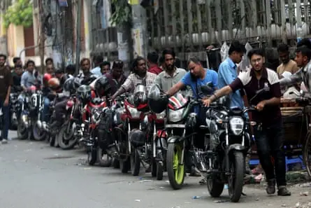 A long line of men pushing motorbikes along a road