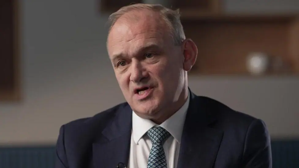 Head and shoulders shot of Davey, who is wearing a navy siut jacket, a white shirt and a blue and green patterned tie.