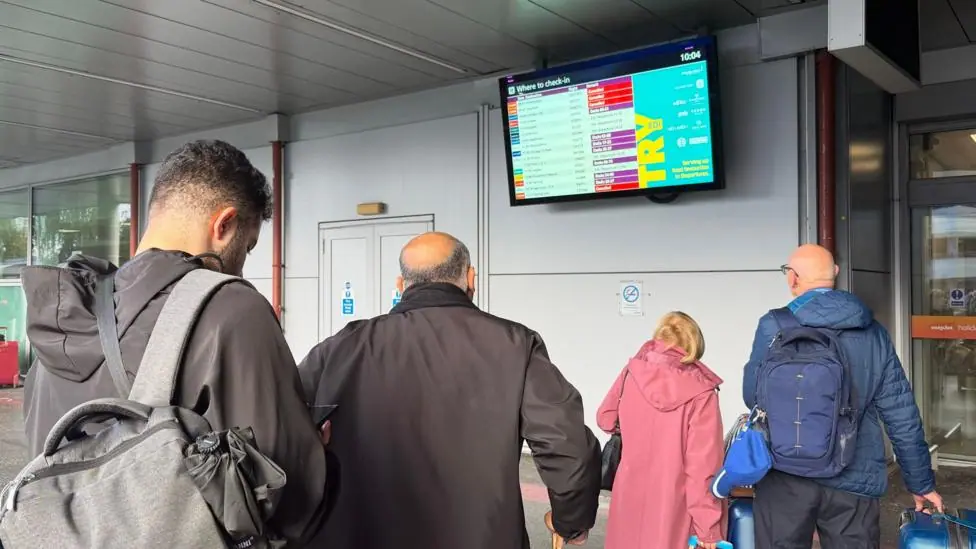 Passengers looking at a airport departure board which has cancellations on it.