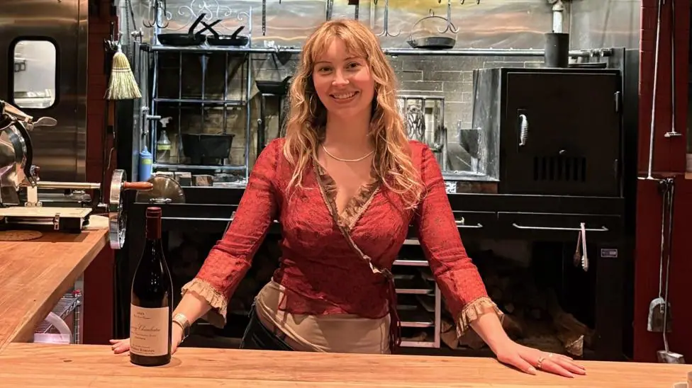 Caroline Kraetzer stands behind a bar, with her hands on the counter.