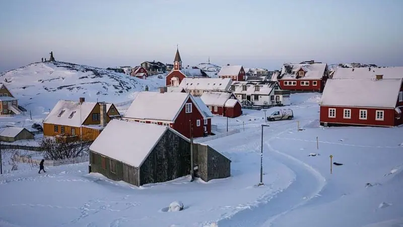 Snow covers houses in Nuuk, Greenland. Some houses are red, with a church in the background