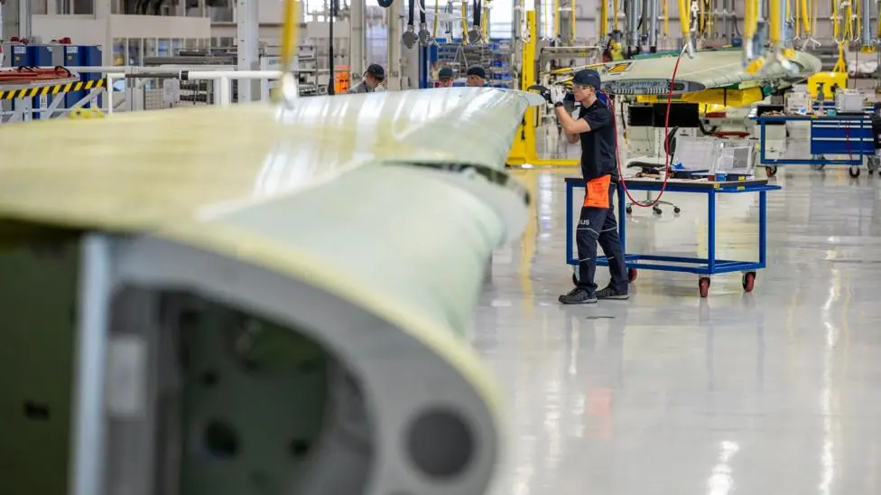 A plane wing is being worked on by an employee in an aerospace facility.
