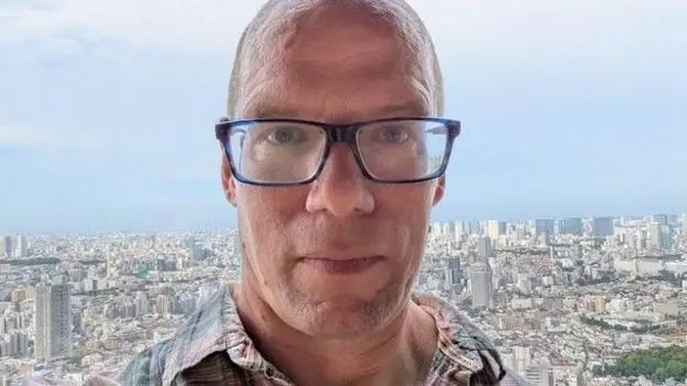 Man in glasses with cityscape behind him