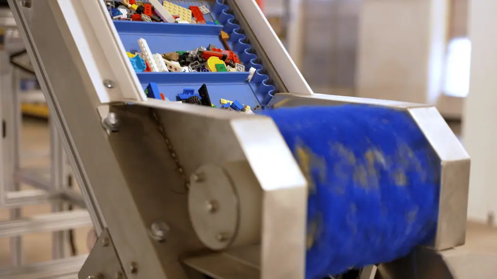 Multicoloured Lego pieces travel along a blue conveyor belt inside an industrial sorting machine.