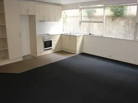 The kitchen and lounge room of a unit with windows that look out at a concrete wall