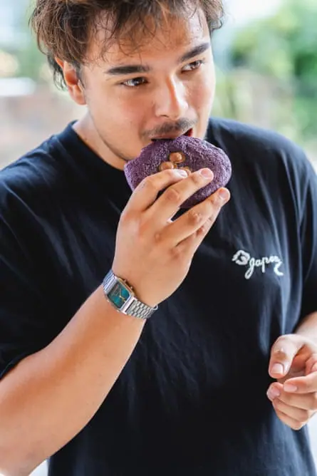 Young man eating a purple cookie.