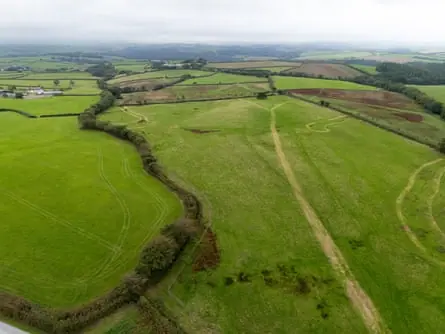 An aerial view of lush green English countryside, with hedges, trees and tracks visible
