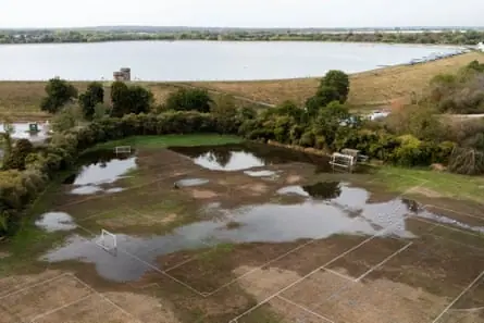 Aerial view of large puddles of water on recreation field, with reservoir behind