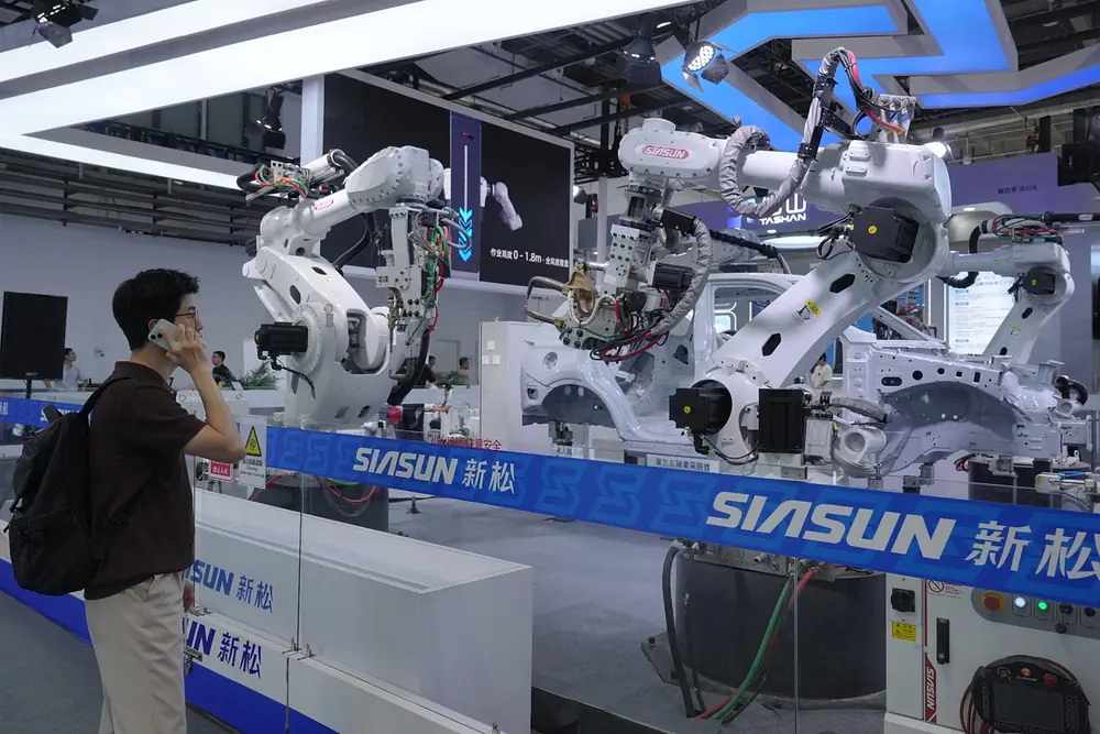 FILE. A visitor looks at robotic arms for industrial production at the World Robot Conference in Beijing, 19 Aug. 2026