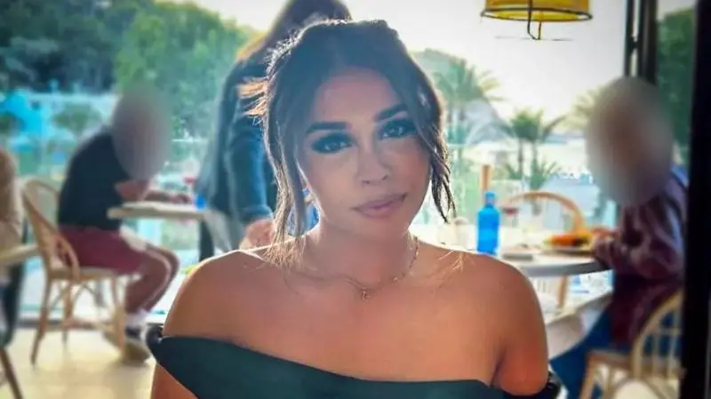 Ravika sitting in a restaurant, pictured head and shoulders looking directly at the camera. She has her hair tied up and is wearing a black off-the-shoulder dress.