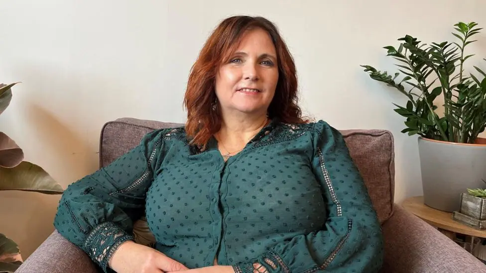 Jill Williams has brown hair and wears a dark green shirt. It is a head and shoulders shot.