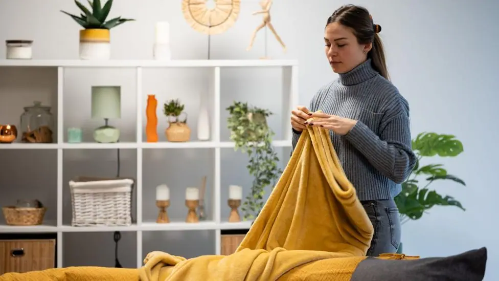 Woman arranging a warm, soft yellow blanket on a sofa