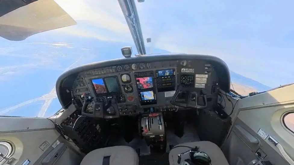 The cockpit of a flying plane with no pilots - just two empty seats.