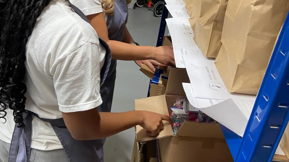 Volunteers at Pelican Parcels check shelved cardboard boxes of school supplies for school children in need.
