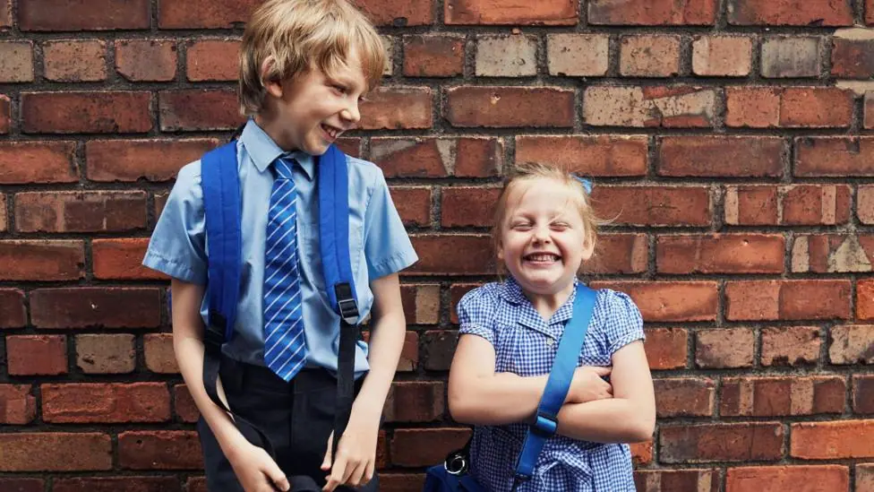 Two happy smiling school children on their way to school wearing blue school uniforms