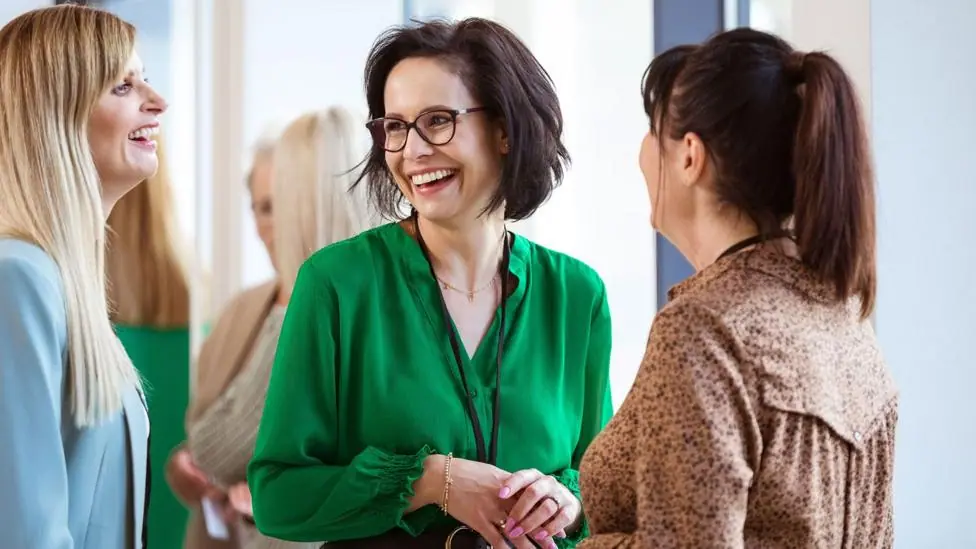 Three middle-aged female colleagues stand in a group, laughing together