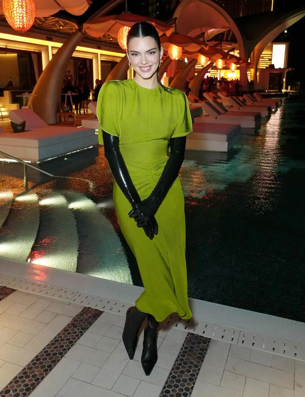 Jenners smiles and clasps her hands while looking at the camera wearing the midi dress, with black gloves and black shoes inside a Dubai hotel.