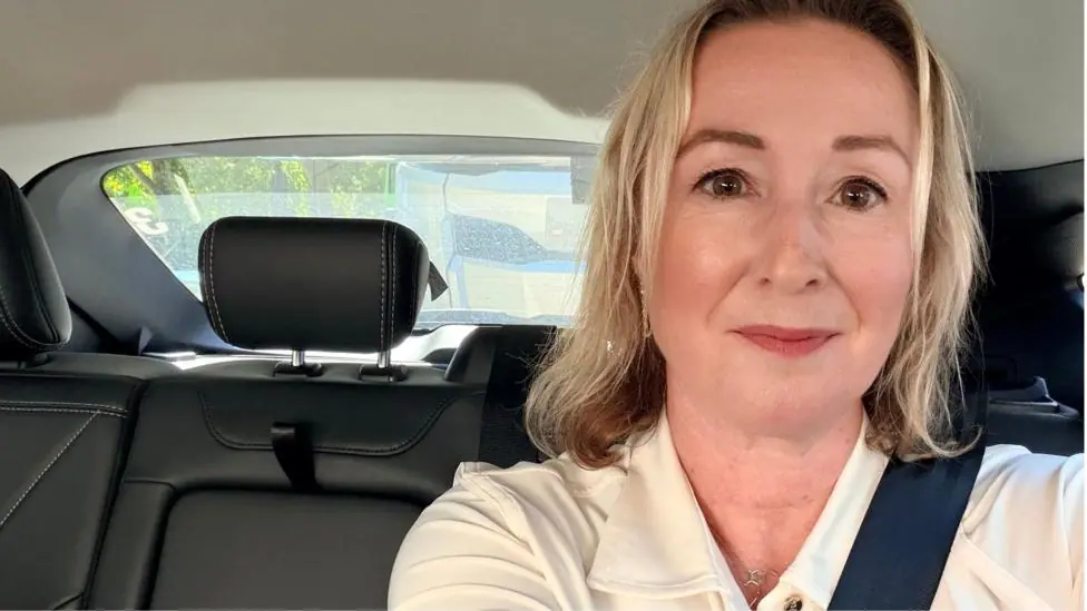 A selfie of Zoe in the back of a driverless robotaxi, wearing a cream blouse and wearing a seatbelt.