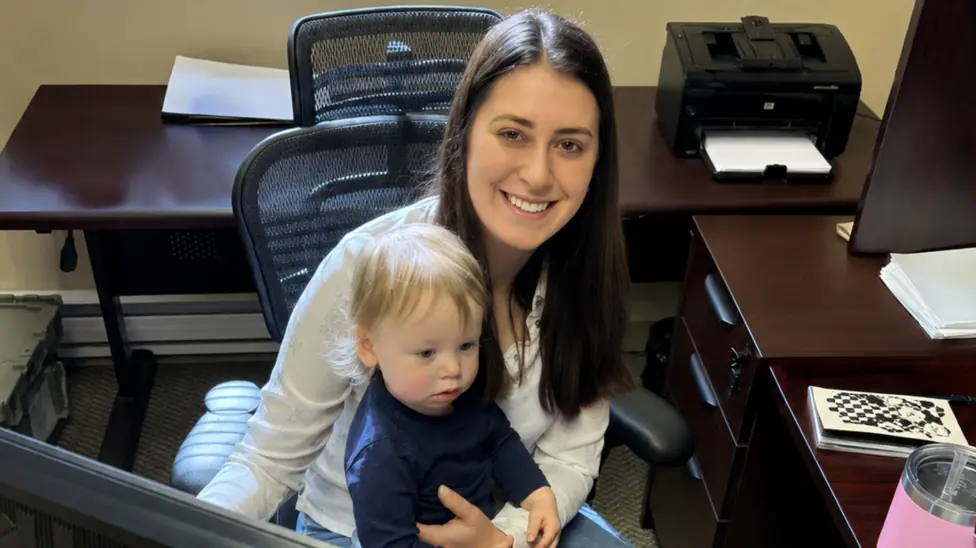 Ania Aliev holds her young son as she sits at her desk