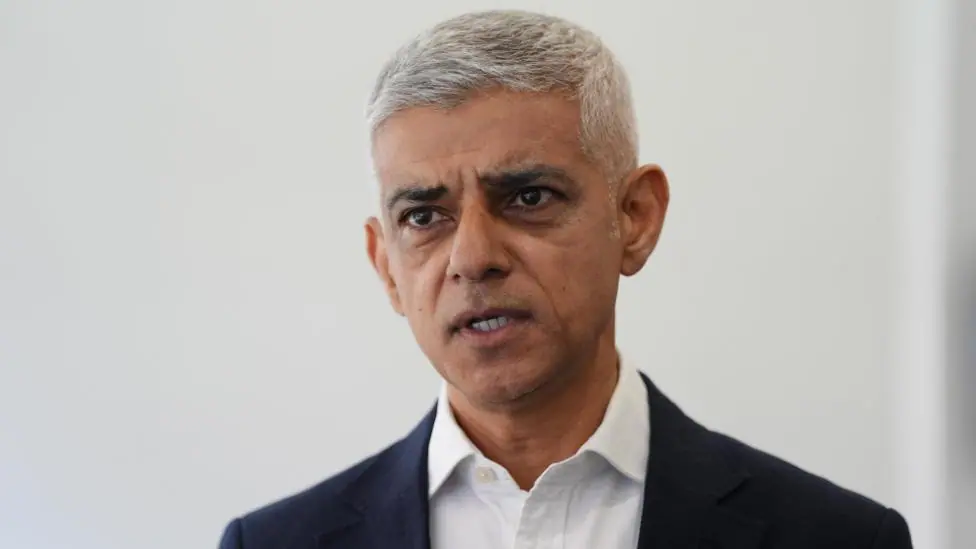 A close-up of Sadiq Khan wearing a dark suit and open-collared white shirt.