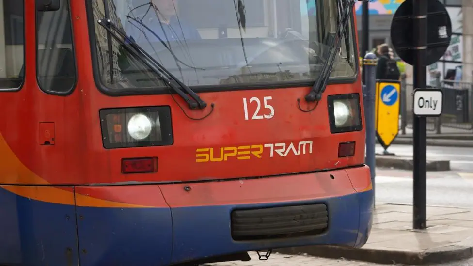 A street scene with a close-up picture of a tram, showing the cab which is painted red and blue and has the number 125 and the word Supertram on the front in capital letters.