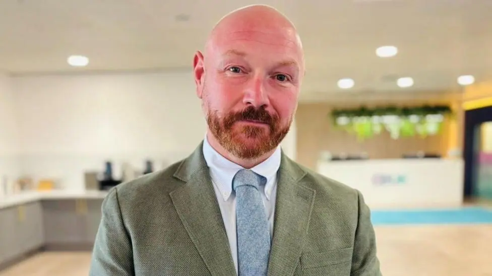 Graham Skinner, a man with a beard, wearing a suit, shirt and light blue tie, looking at camera.