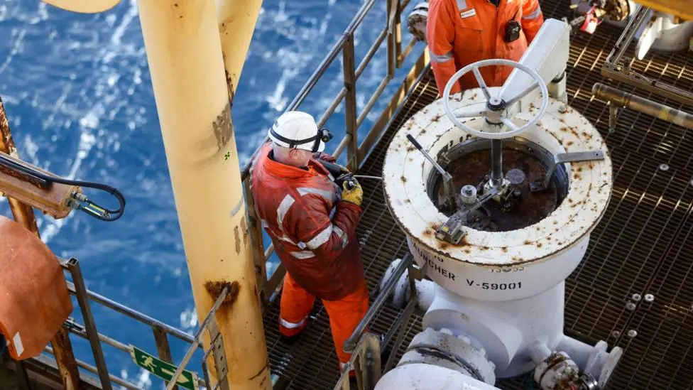 Two workers wearing orange overalls and a hard hats fix a pig launcher on the Armada gas condensate platform, operated by BG Group Plc, in the North Sea, off the coast of Aberdeen.