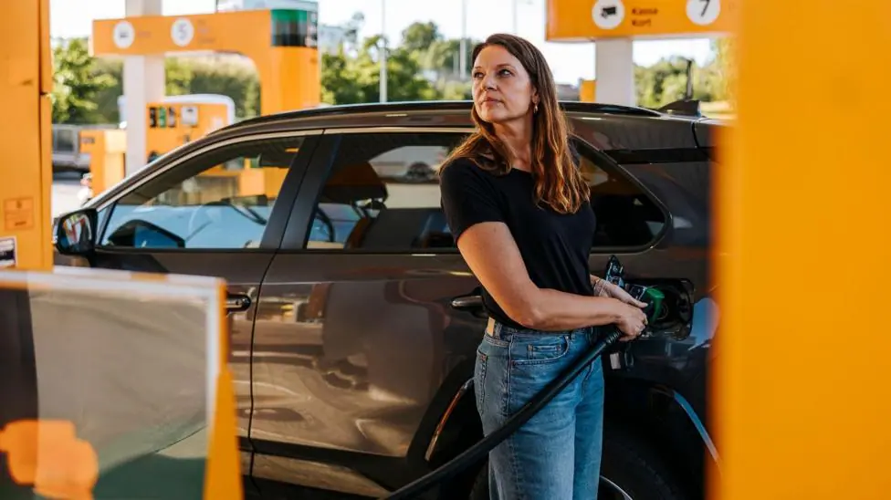 Stock photo shows a woman filling up her car with petrol at a station with yellow pumps